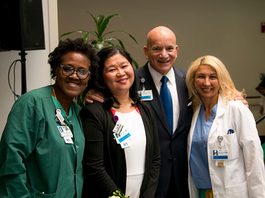 A man standing next to three woman health professionals, they all smile at the camera