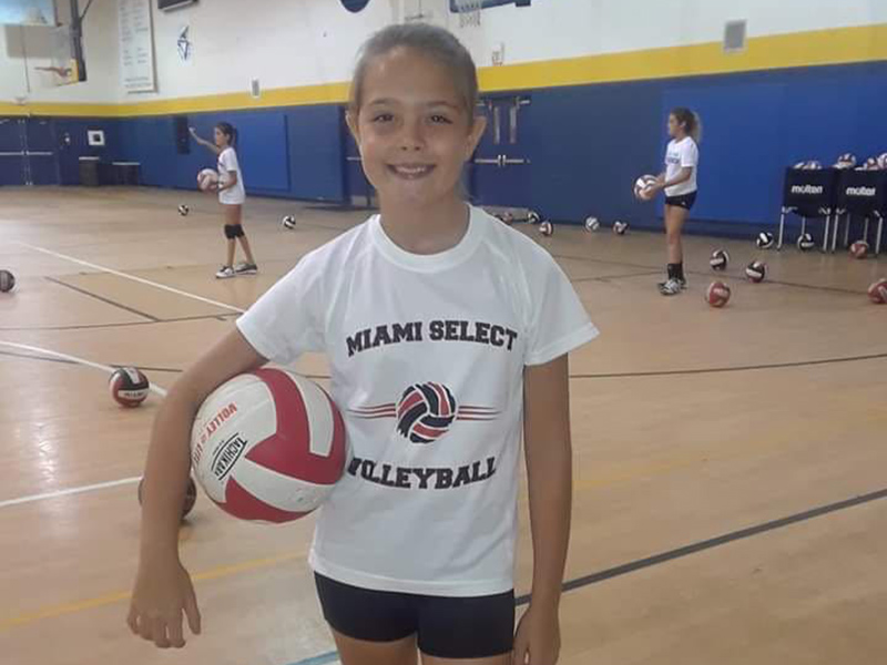 Victoria Bermudez at a volleyball game, she is holding a volley ball between her right arm and hip