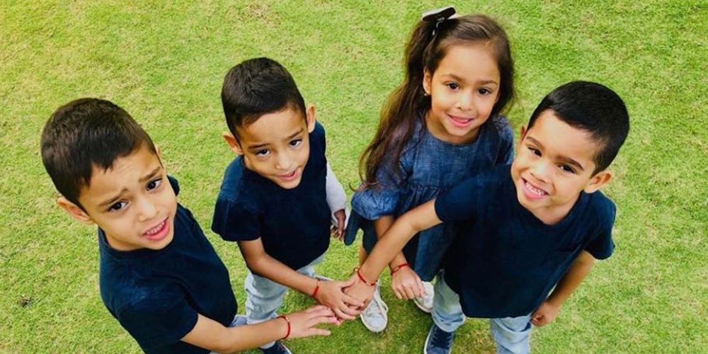 Gutierrez quadruplets standing next to each other, there are three boys and one girl, they are placing their hands in the middle