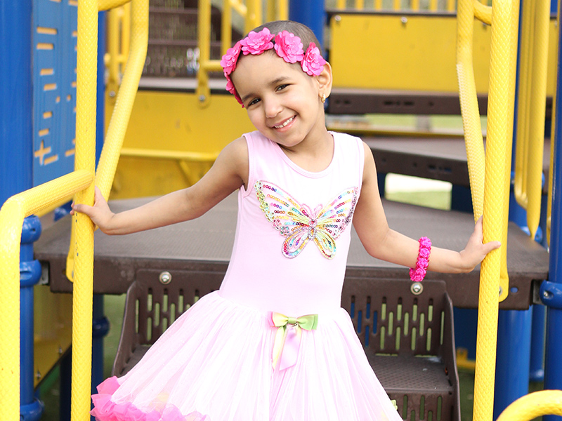 Salma in a playground smiling, she is wearing a pink ballet dress and a flower crown