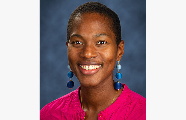 Woman smiling at the camera, she is wearing a fuchsia blouse and aqua colored earrings