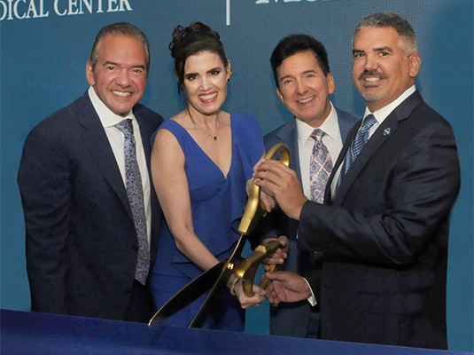 Group of three men and a woman cutting a blue ribbon with large scissors