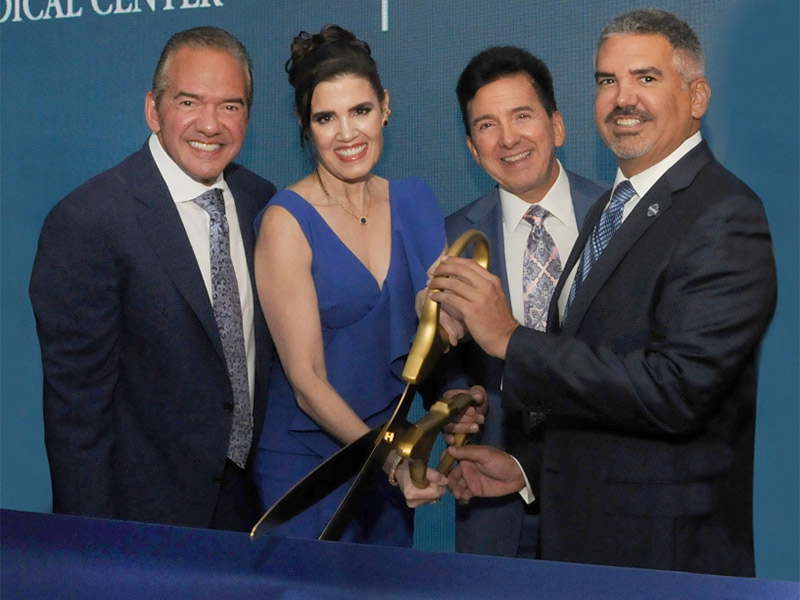 Group of three men and a woman cutting a blue ribbon with large scissors