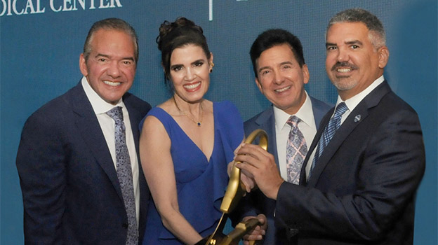 Group of three men and a woman cutting a blue ribbon with large scissors