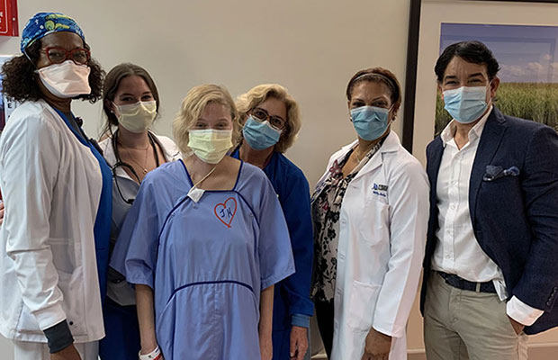 A group of medical professionals, a man, and a patient within a hospital hallway. They are all wearing face coverings and looking at the camera