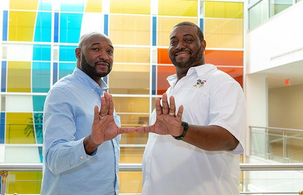 Two man smiling at the camera, they put their hands together to form a U