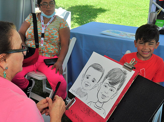 A child smiling, there is a woman drawing a caricature