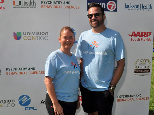 A woman and man standing in front of a step and repeat, they have on light blue shirts
