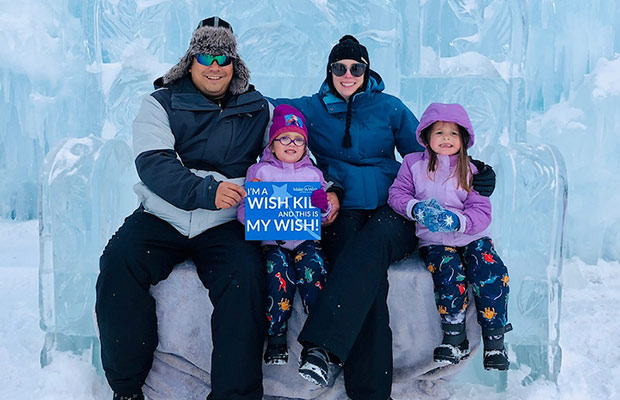 A mom and dad sitting on an ice sculpture with their two young daughters; there is a sign that reads I'm a wish kid and this is my wish!