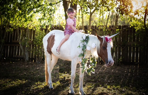 Young girl on a horse, the girl smiles at the camera, the horse has flowers around its neck