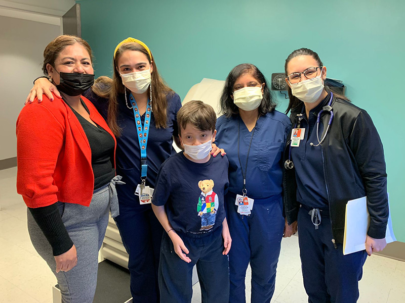 A group of medical professionals, a woman, and a young boy, they all look towards the camera, they are all wearing face masks