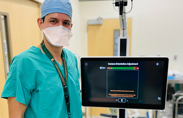 A healthcare professional standing next to a machine, he is wearing scrubs, a face mask, and a hair cap