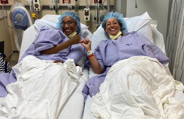 Two women laying on separate medical meds, they smile at the camera and have their pinkies locked together