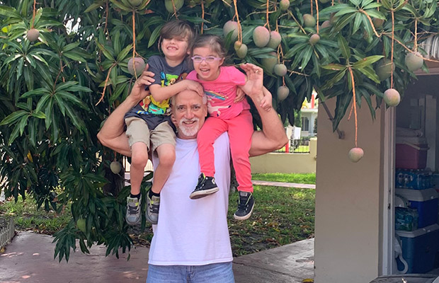 A middle aged man holding two young children on his shoulders, they're all smiling at the camera