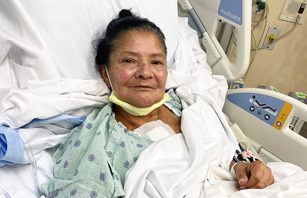 A woman wearing a hospital gown, she is laying on a medical bed