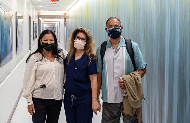 Two people and a medical professional standing in a hallway, they look at the camera