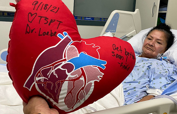 A woman in a medical bed, wearing a gown, she is receiving a heart shaped pillow