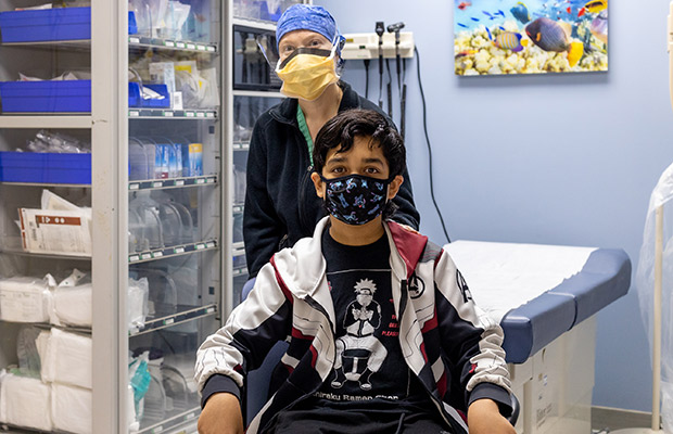 A young patient sitting down next to a medical professional who is standing behind him