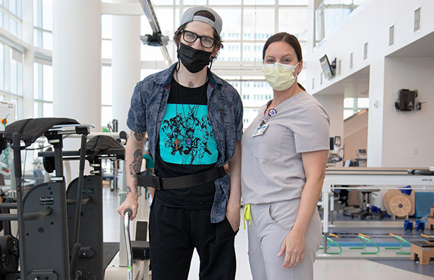 A young man wearing a face mask and holding a cane standing next to a medical worker who also wears a face mask