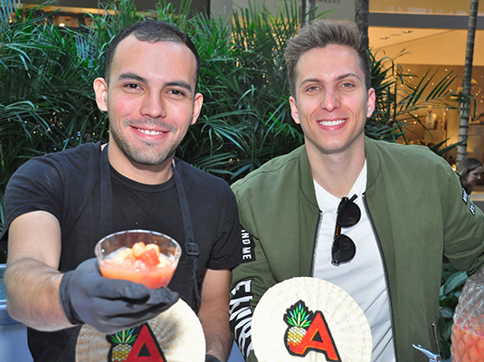 Two men smiling at the camera, one holds up a cup