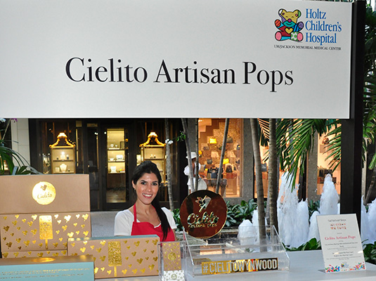 A woman standing behind a booth, the sign above her reads Cielito Artisan Pops