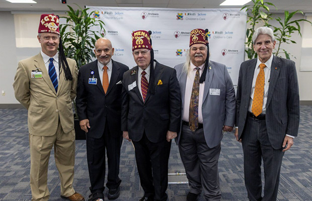 Five men standing next to each other, they are indoors and all look at the camera