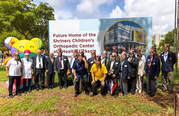 A large group of people standing outdoors, they are standing in front of a large colorful bear and sign