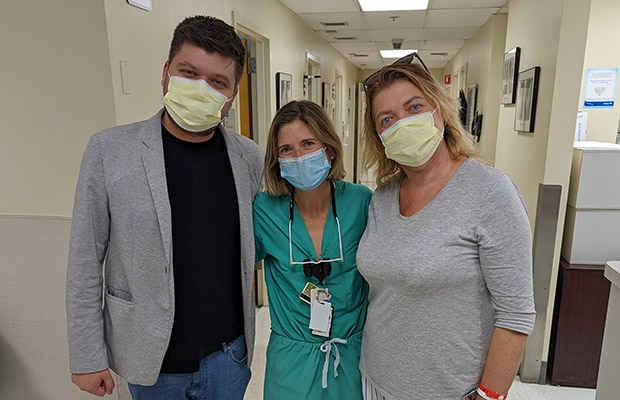 A man and woman standing next to a medical professional, they all have face masks and are looking at the camera