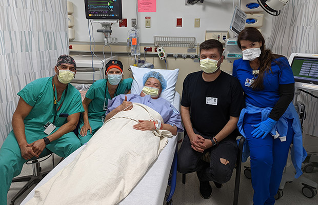 Medical professionals, a patient, and guest in a medical room, they all have on face masks and look at the camera