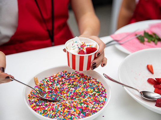A closeup of a person scooping sprinkles into an ice cream cup