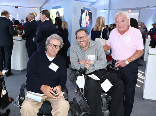 A group of three men smiling, there are more people behind them at an event