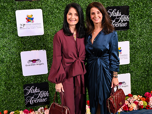 Two women smiling at the camera, they stand in front of a step and repeat