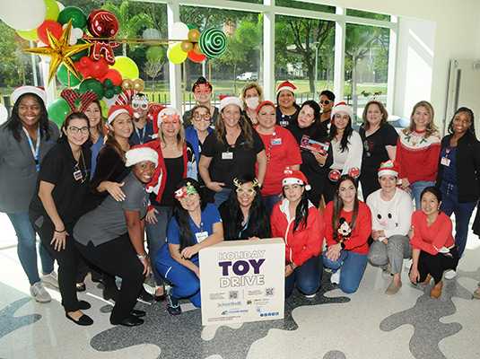 A large group of people standing behind a sign that reads holiday toy drive
