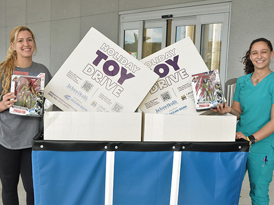 Two women holding toys next to signs that read holiday toy drive