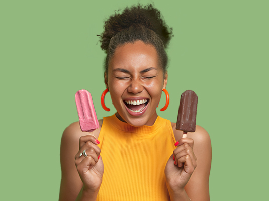 A woman smiling with her eyes closed, she is holding a popsicle within each hand