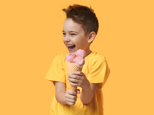 A young boy smiling, he is holding on to a large ice cream cone filled with scoops of ice cream