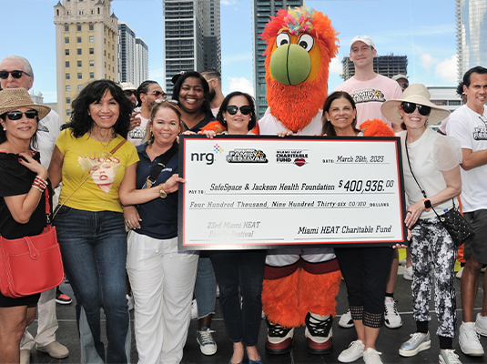 group of people posing for the camera next to a puppet holding a giant check