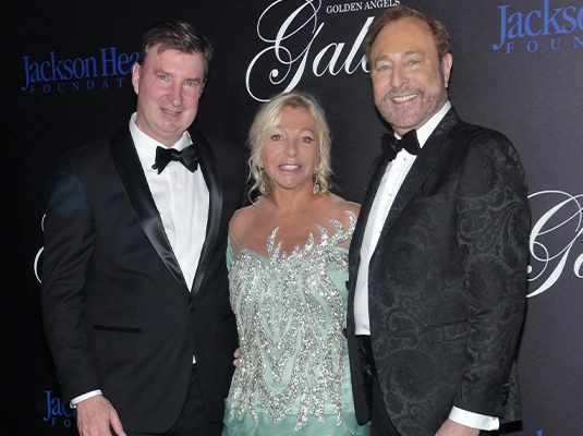 Three people posing and smiling at the camera at a gala event