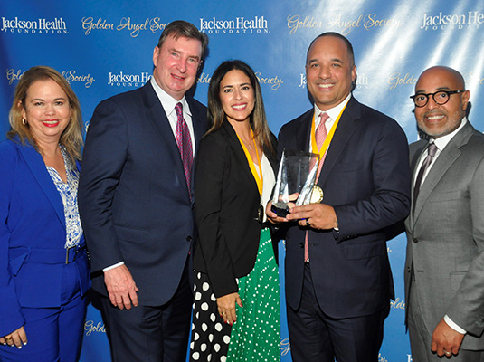 Five people smiling at the camera, one man holds up an award