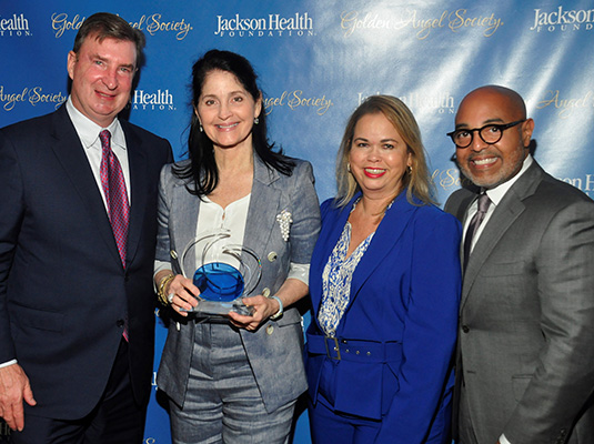 Four people smiling at the camera, one woman holds up an award