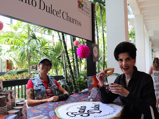 women smiling at the camera while eating churro and coffee