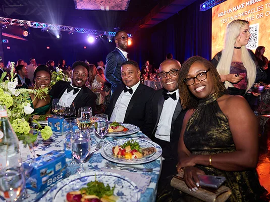 Group of people sitting around a table at a gala, they smile at the camera