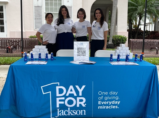 group of four women behind a table with a blue tablecloth that has the one day for jackson logo printed on it