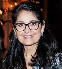 A woman with long dark hair and black trimmed glasses smiles at the camera