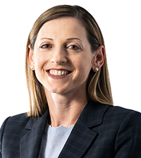 A woman with light brown hair smiles at the camera, she has on a suit jacket and light blue shirt