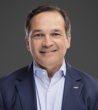 A man smiles at the camera, he has on a suit jacket and collared shirt