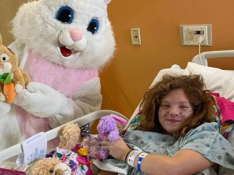 A girl in a hospital bed with a person in a rabbit garment