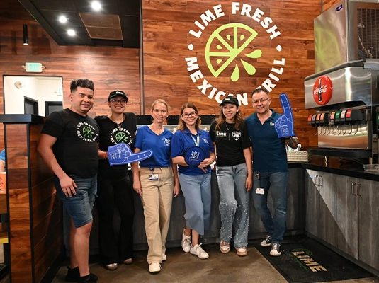 Five people smiling and posing for the camera in a restaurant