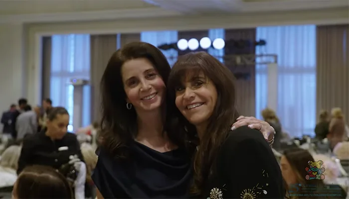 Two women smiling and looking at the camera, they're wearing dark clothing and are at an event