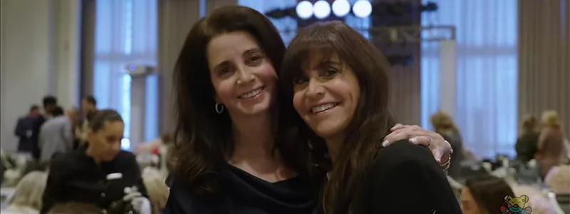 Two women smiling and looking at the camera, they're wearing dark clothing and are at an event